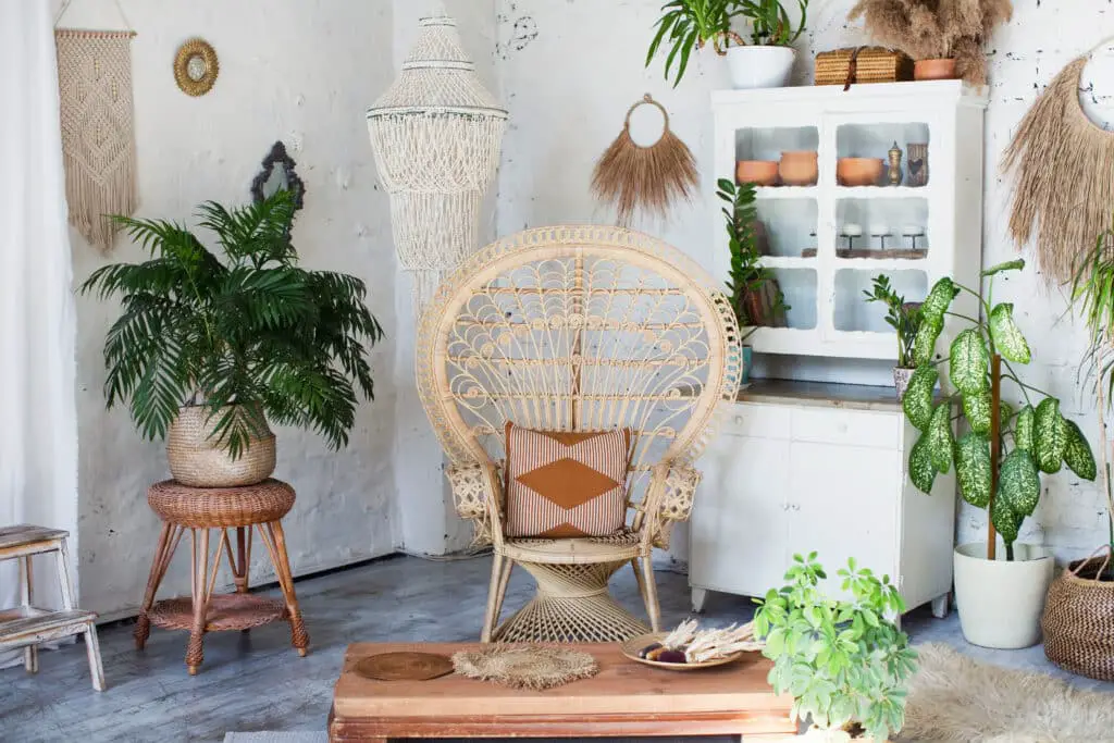 Bohemian stylish interior with peacock armchair, green plants in flowerpots and vintage boho details