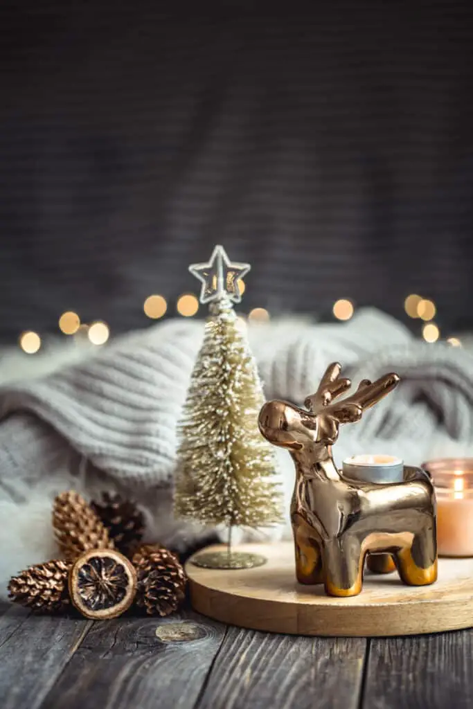 Christmas festive background with toy deer, blurred background with golden lights and candles, festive background on wooden deck table and winter sweater on background