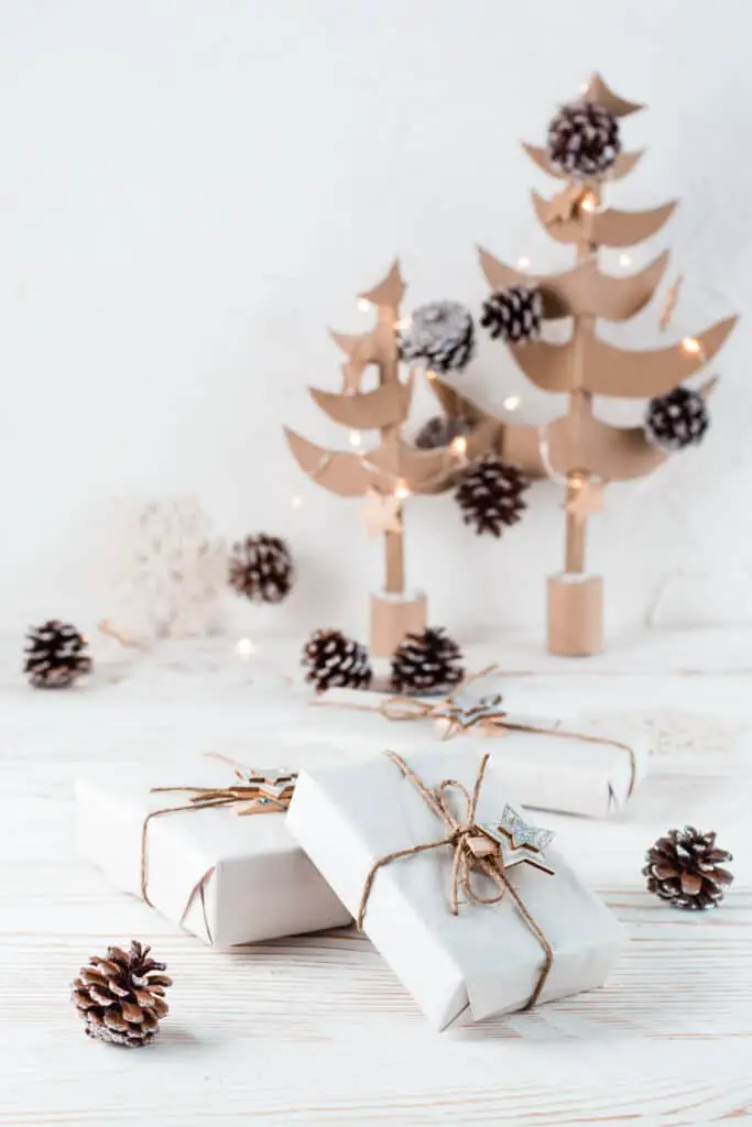 Christmas gifts wrapped in craft paper tied with twine on the background of Christmas fir trees made of cardboard on a wooden table. Organization of an eco-friendly holiday. Vertical view
