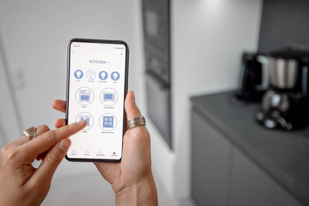 Smart phone with running mobile application to control smart devices in the kitchen. Female controlling smart devices with phone at home. Smart home concept